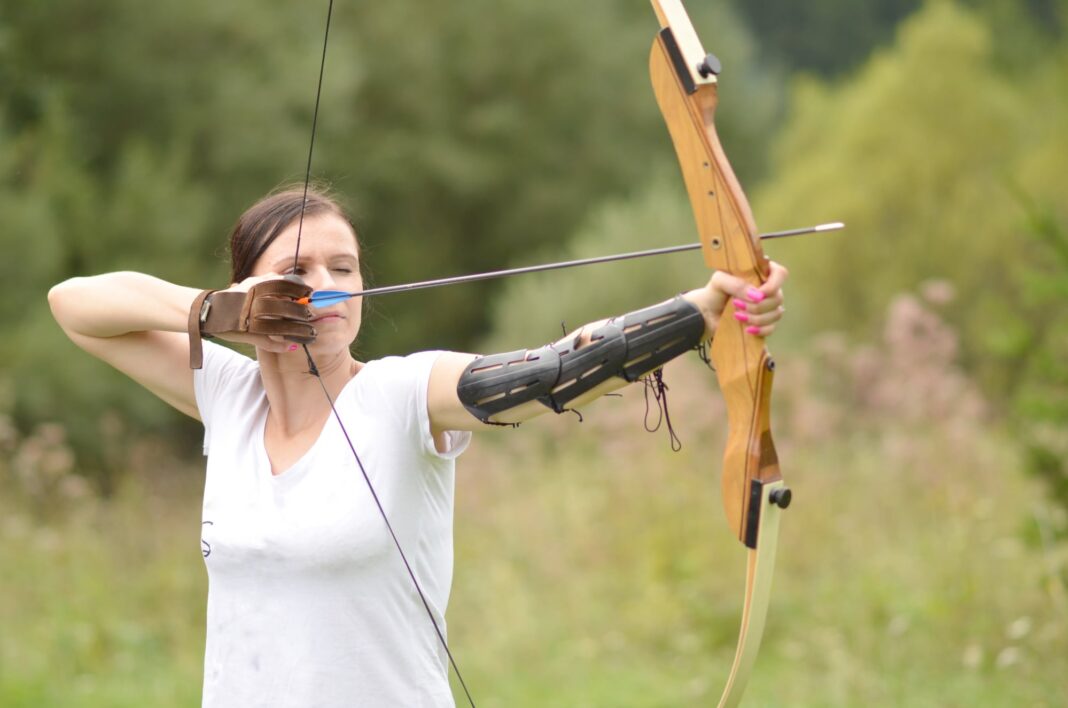 Persona practicando tiro con arco en un campo de tiro, con el arco tensado y apuntando al blanco.