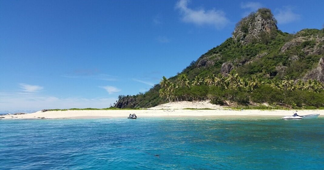 Fotografía aérea del crucero MV Fiji Princess encallado en aguas cercanas a una isla tropical con arrecifes visibles.