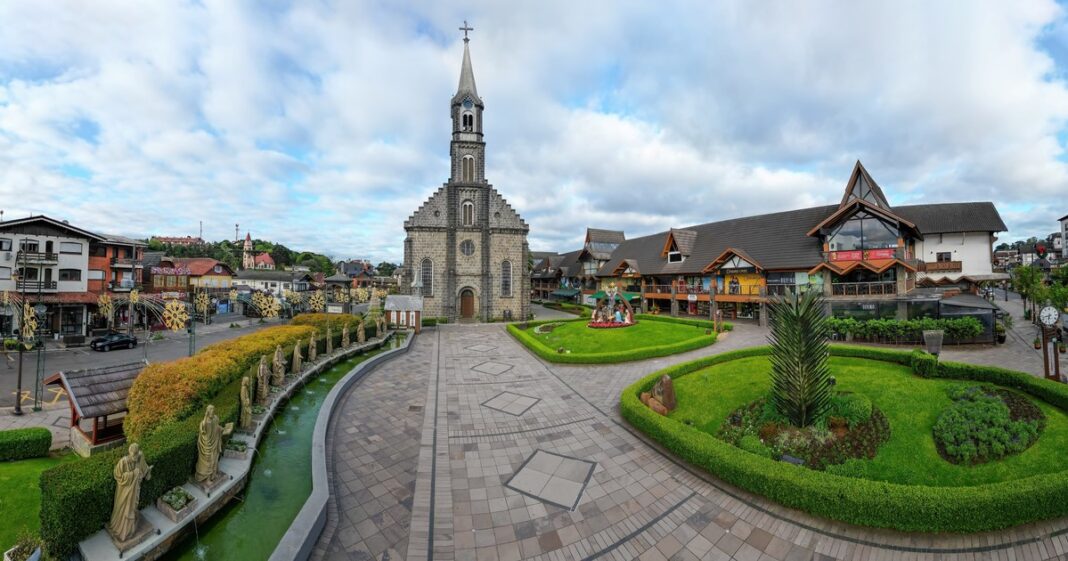 Vista de la arquitectura alpina y calles decoradas de Gramado, Brasil, con montañas verdes de fondo.
