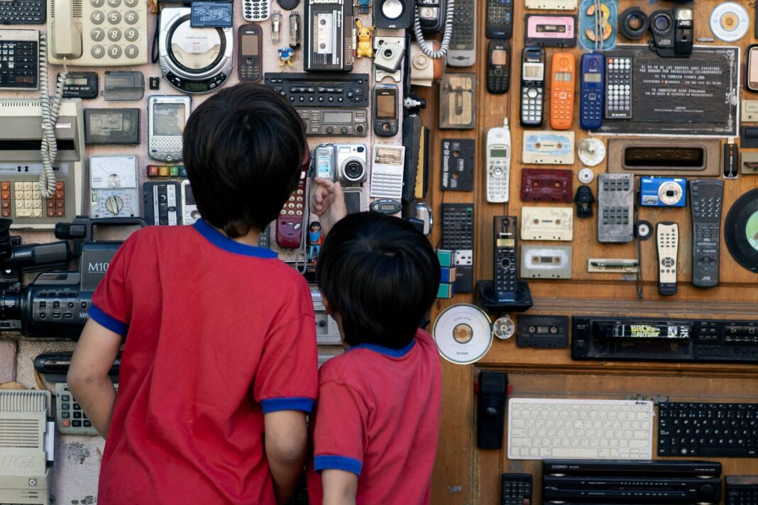 Dos niños observan una instalación con walkmans, discmans y otros dispositivos antiguos en la fachada de una casa en Buenos Aires