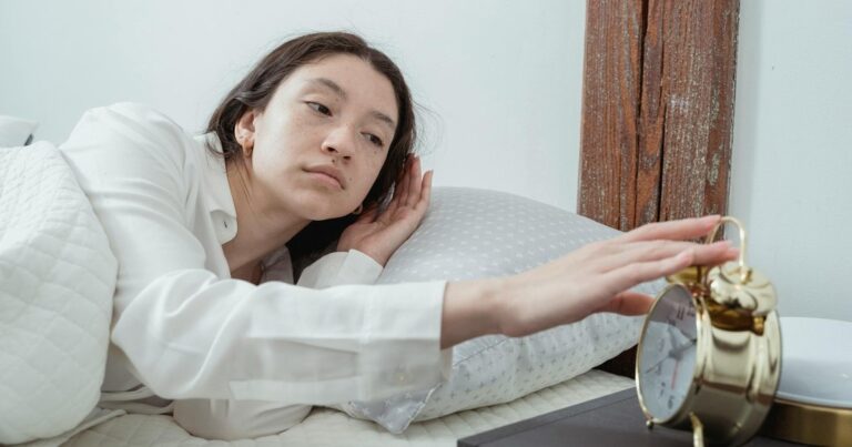 Persona despertándose con luz natural de la mañana junto a un reloj de alarma, representando la importancia de un horario fijo.