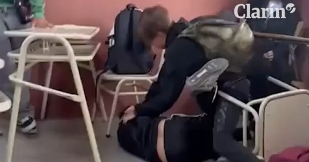 Grupo de adolescentes conversando en un entorno escolar, con un adulto observando a lo lejos.