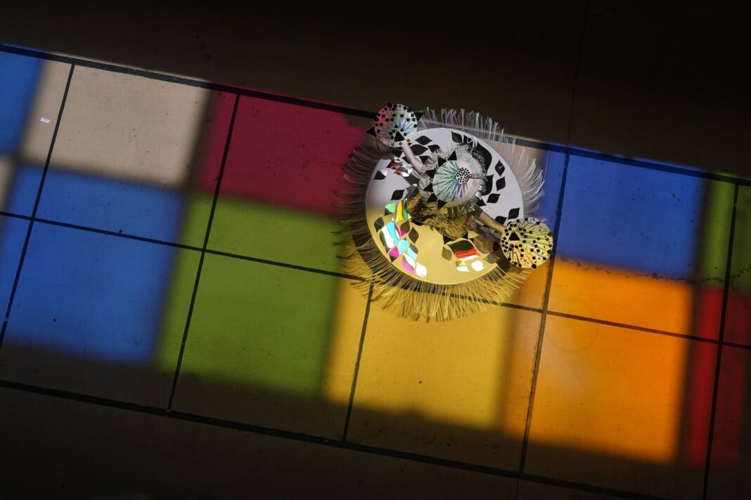 Toma cenital de la bailarina Catherine Cisneros bailando sobre reflejos de colores en el piso del Aeropuerto Internacional de San Antonio durante el solsticio de verano