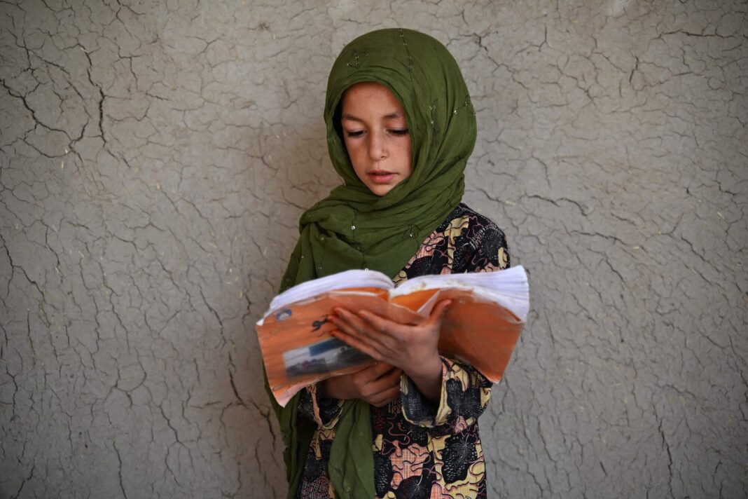 Niña con hiyab verde leyendo un libro en una escuela de Kandahar, Afganistán